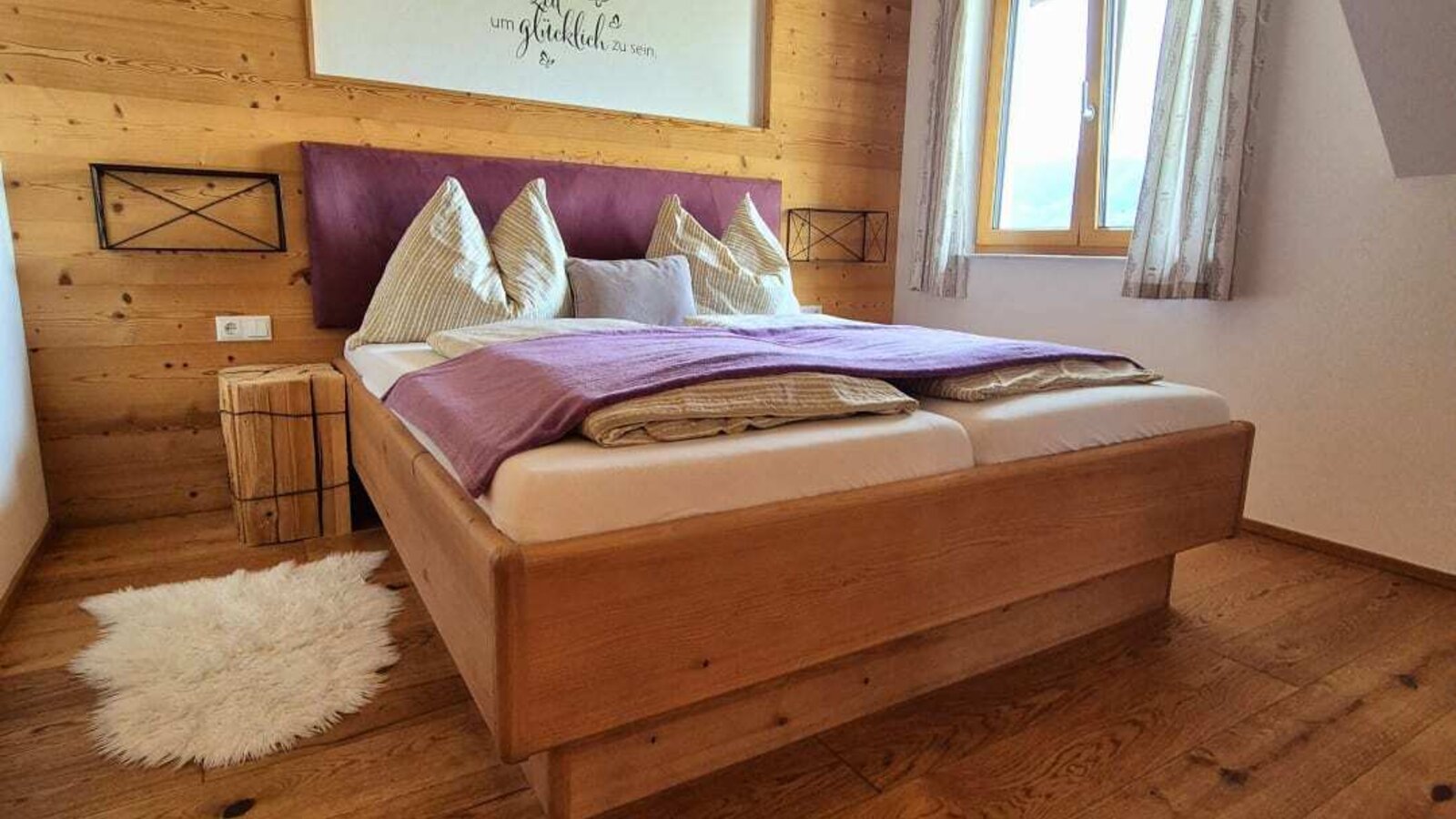 Schlafzimmer im Bauernhof mit Doppelbett, Holzwänden, Holzboden und einem Fenster.