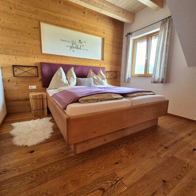 Schlafzimmer im Bauernhof mit Doppelbett, Holzwänden, Holzboden und einem Fenster.