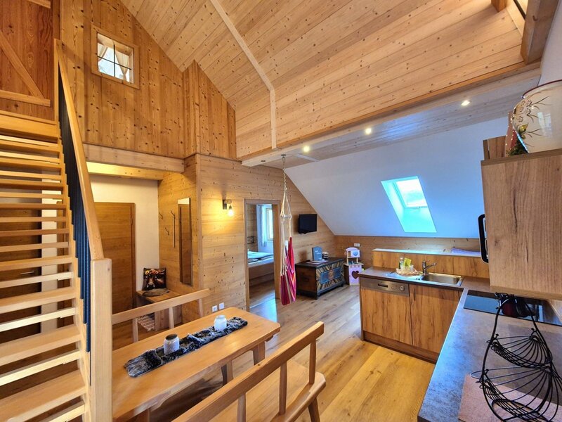 Der Wohnbereich des Bauernhofs mit Holztisch, integrierter Küche und Treppe zum oberen Stockwerk.
