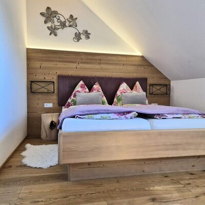 Schlafzimmer im Bauernhof mit Holzbett, Holzwandverkleidung und Dachschräge.