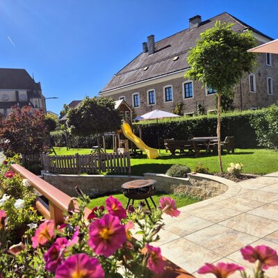 Der Garten des Bauernhofs mit Spielplatz, Rutsche, Picknicktisch und gepflasterter Terrasse, umgeben von Blumen.