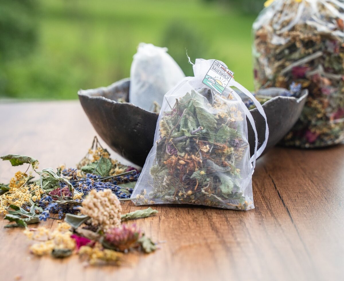 Hofeigene getrocknete Kräuter und Kräutermischungen, teils in Säckchen verpackt, auf einem Holztisch.