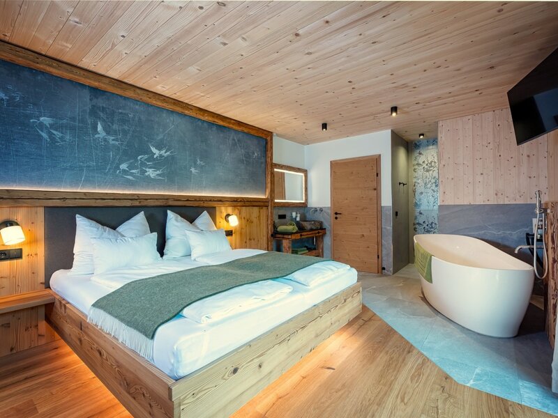 Schwalbenzimmer im Chalet mit freistehender Badewanne, Holzelementen und Wandfernseher.
