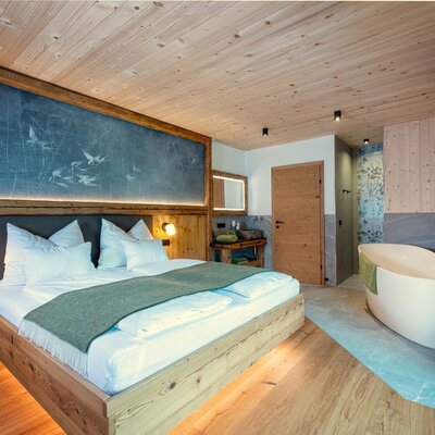 Schwalbenzimmer im Chalet mit freistehender Badewanne, Holzelementen und Wandfernseher.
