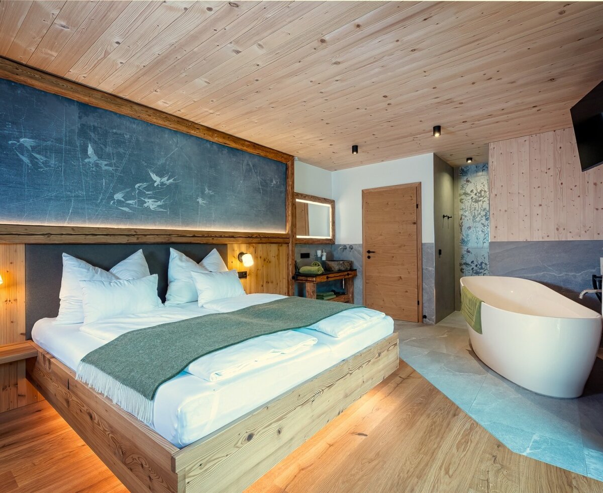 Schwalbenzimmer im Chalet mit freistehender Badewanne, Holzelementen und Wandfernseher.