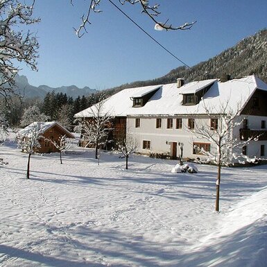 Der Bauernhof im Winter, mit schneebedecktem Gartenbereich und Bergblick.
