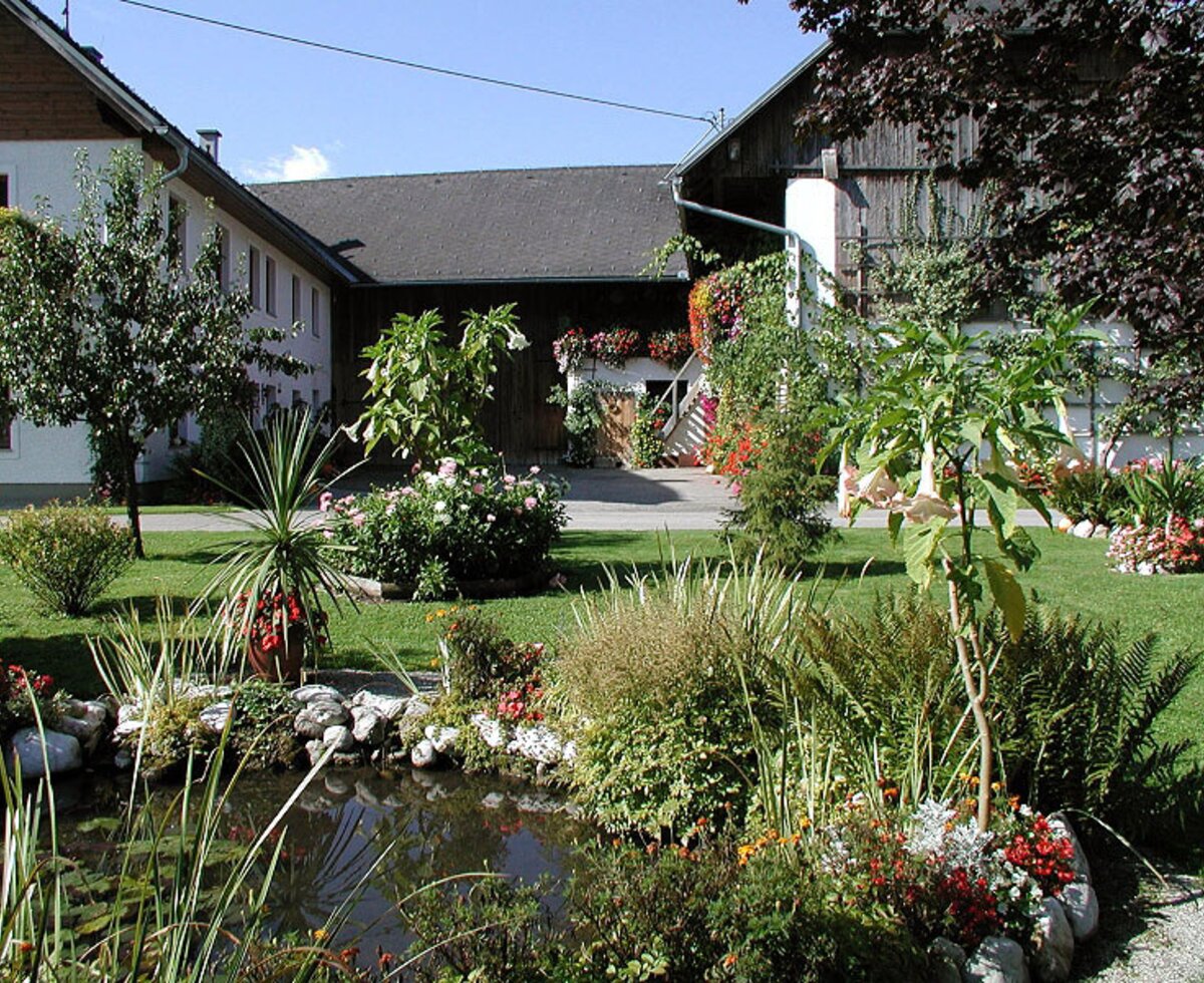Der Garten des Bauernhofs mit einem Teich, Blumenbeeten und Grünflächen.