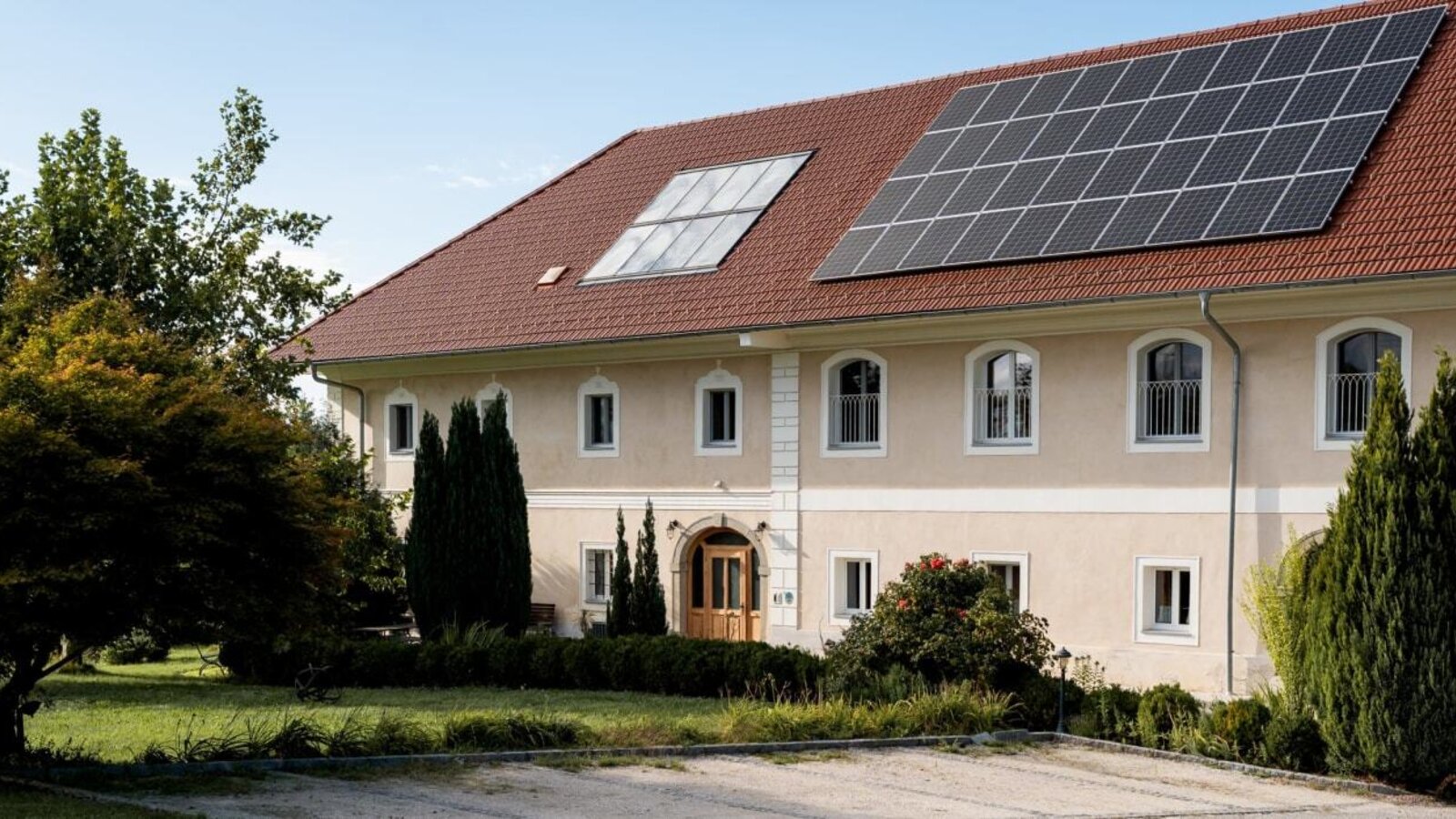 Das einladende Gebäude des Bauernhofs mit einem gepflegten, grünen Garten und modernen Solarmodulen auf dem Dach.