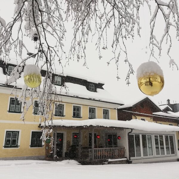 Der winterliche Bauernhof mit schneebedeckten Dächern und Bäumen, geschmückt mit großen goldenen Weihnachtskugeln.