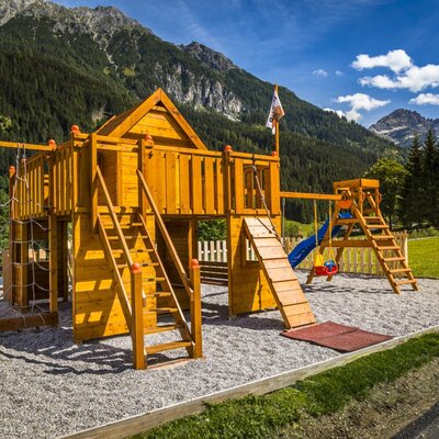 Hölzerner Kinderspielplatz mit Rutsche, Schaukeln und Klettergerüst am Bauernhof.