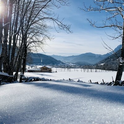 Winterlicher Blick auf die verschneite Berglandschaft und den Bauernhof.