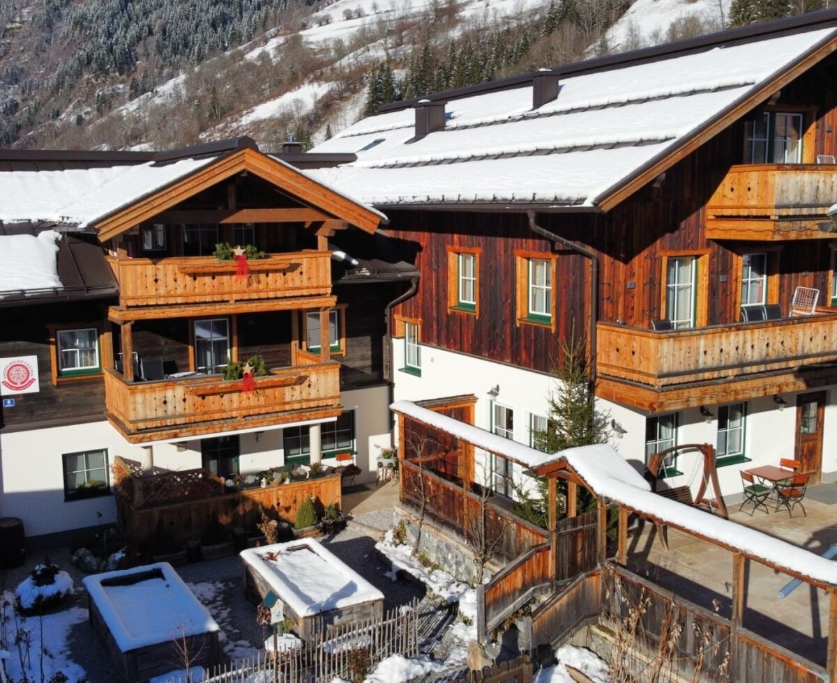 Der Bauernhof im Winter mit verschneiten Dächern, Balkonen und einem Außenbereich mit Sitzgelegenheiten und einem schneebedeckten Whirlpool.