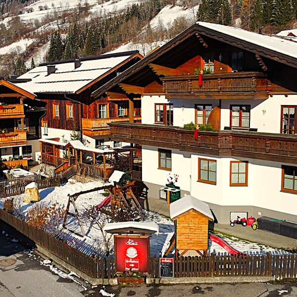 Die Gebäude des Bauernhofs mit Balkonen und einem Kinderspielplatz mit Schaukel und Rutsche im Schnee.