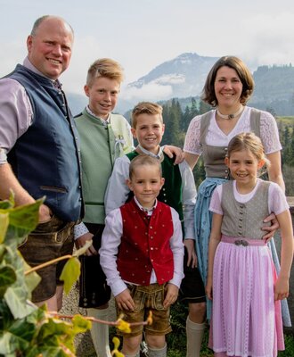 Die Gastgeberfamilie des Bauernhofs in traditioneller Kleidung vor alpiner Kulisse.