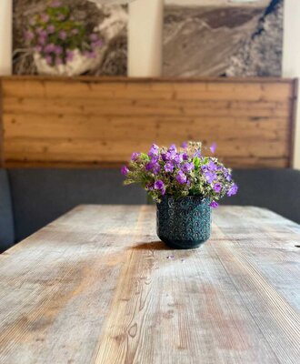 Ein rustikaler Holztisch im Bed and Breakfast, geschmückt mit einer charmanten Vase voller violetter Blumen.