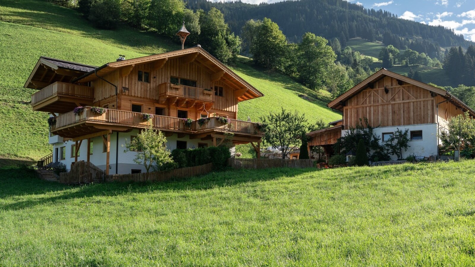 Der charmante Bauernhof eingebettet in eine saftig grüne Wiese vor einer malerischen Bergkulisse.