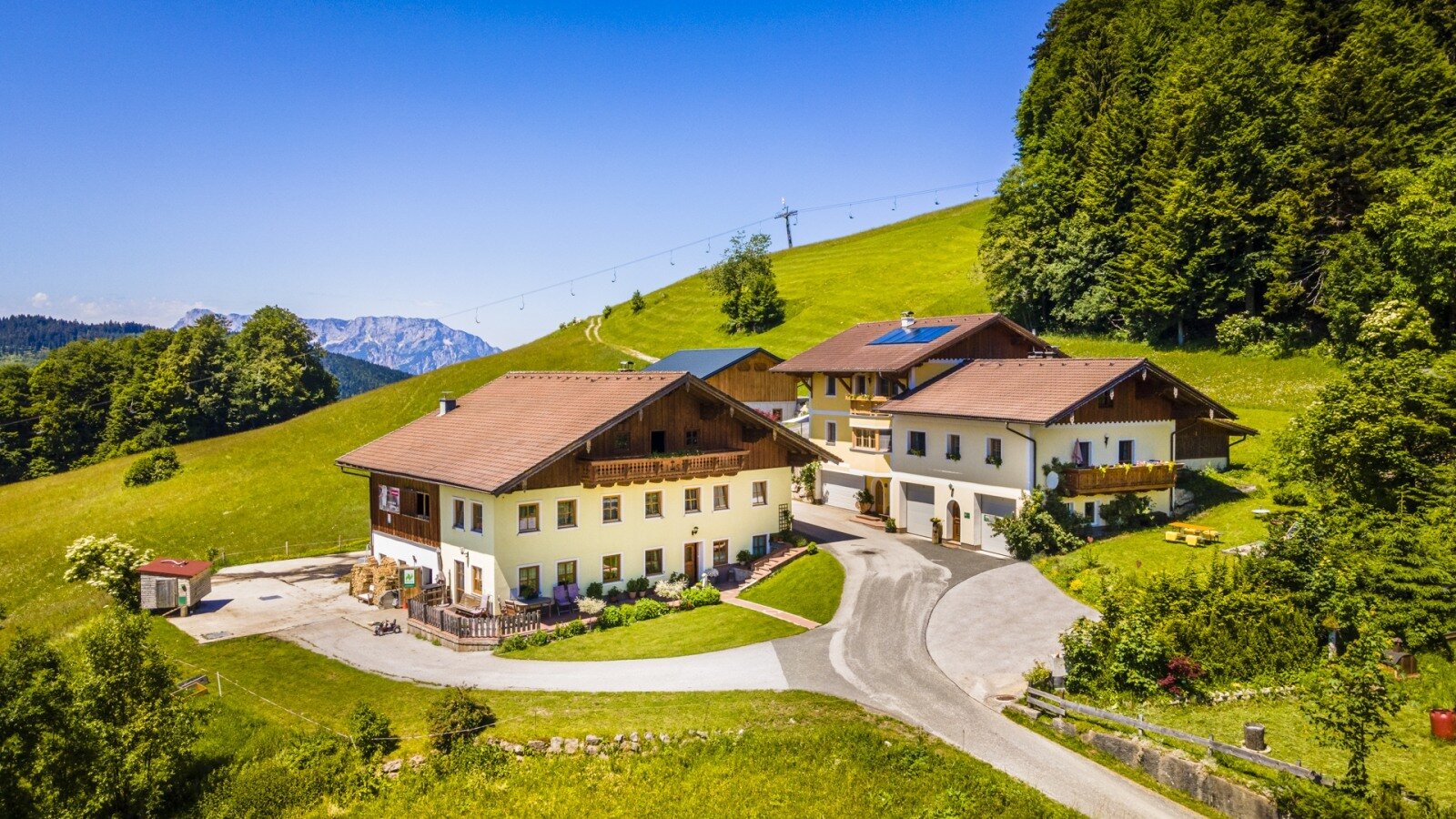 Der Bauernhof Reitlhof mit seinen Gebäuden, gelegen auf einem grünen Hang mit Blick auf die umliegenden Berge.