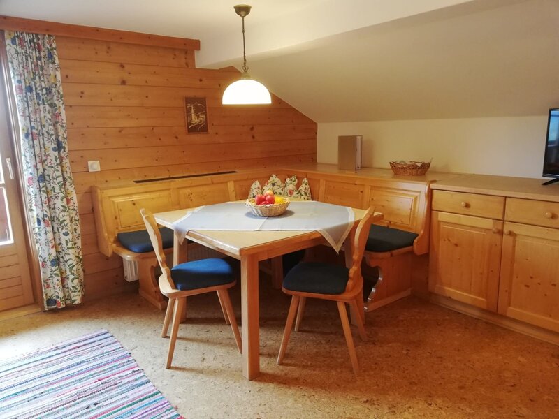 Essbereich im Bauernhof mit Holzeckbank, Esstisch, Stühlen, Holzvertäfelung und einem TV auf dem Holzschrank.