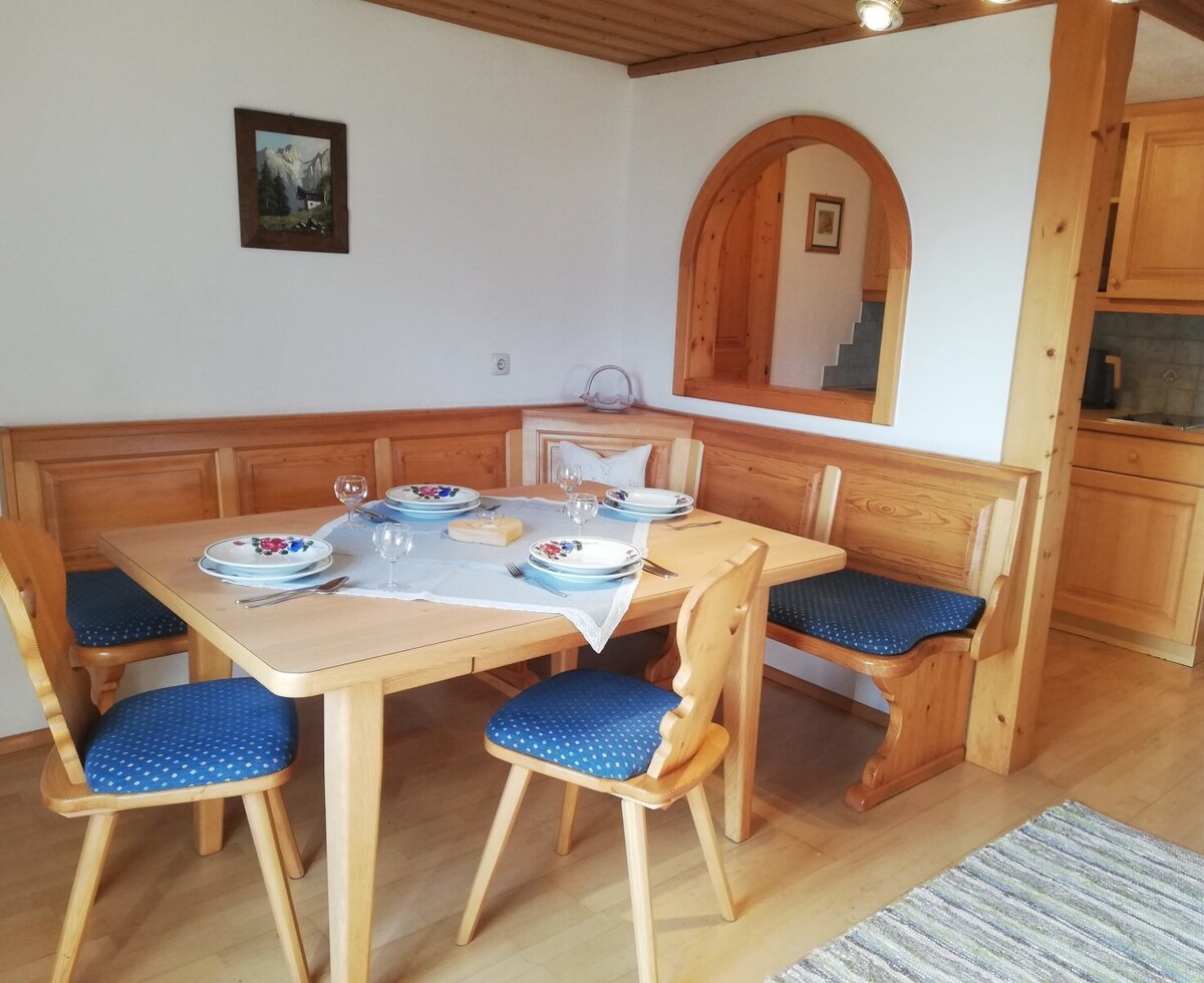 Im Essbereich des Bauernhofs befinden sich ein rustikaler Holztisch mit Eckbank und Stühlen, gedeckt für gemeinsame Mahlzeiten, angrenzend an eine Küchenzeile.