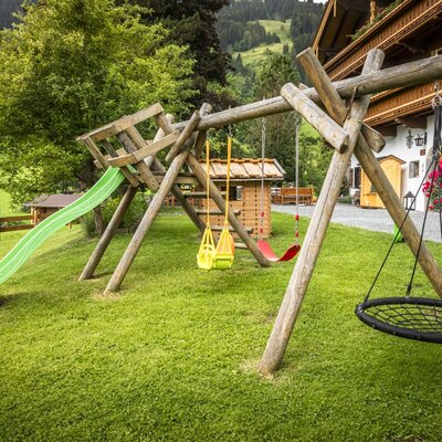 Der einladende Kinderspielplatz des Bauernhofs mit Rutsche, Schaukeln und einem Spielhaus auf einer grünen Wiese.
