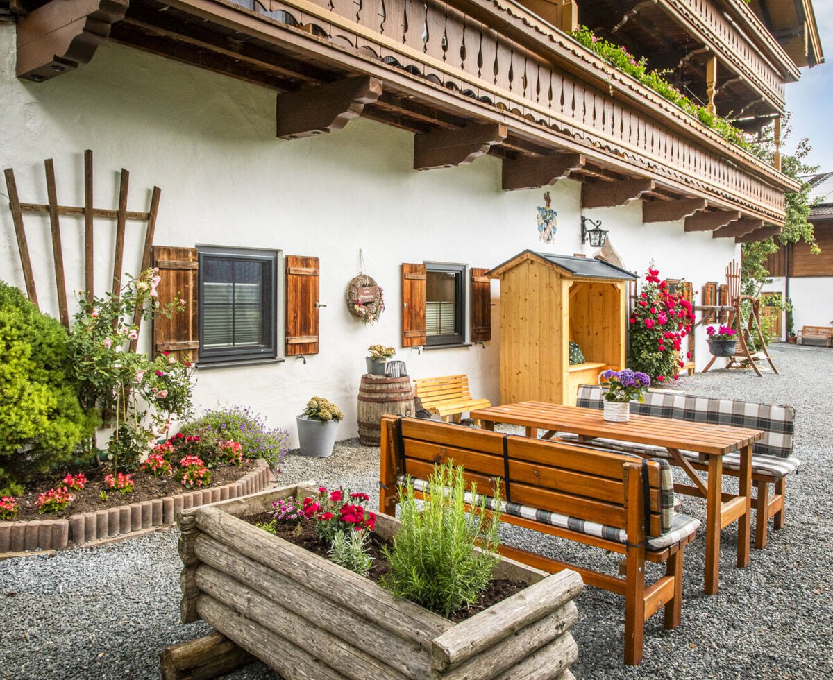Der einladende Außenbereich des Bauernhofs mit gemütlichen Holzbänken und buntem Blumenschmuck.