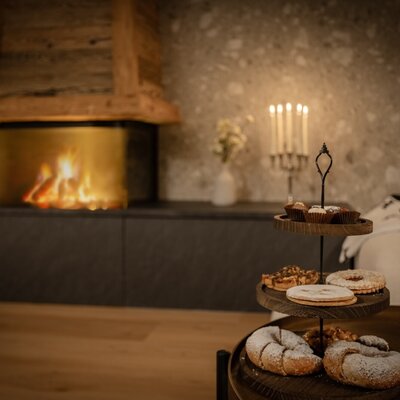 Kamin mit brennendem Feuer, eine Etagere mit Gebäck und Muffins sowie zwei Gläser Rotwein im Bauernhof.