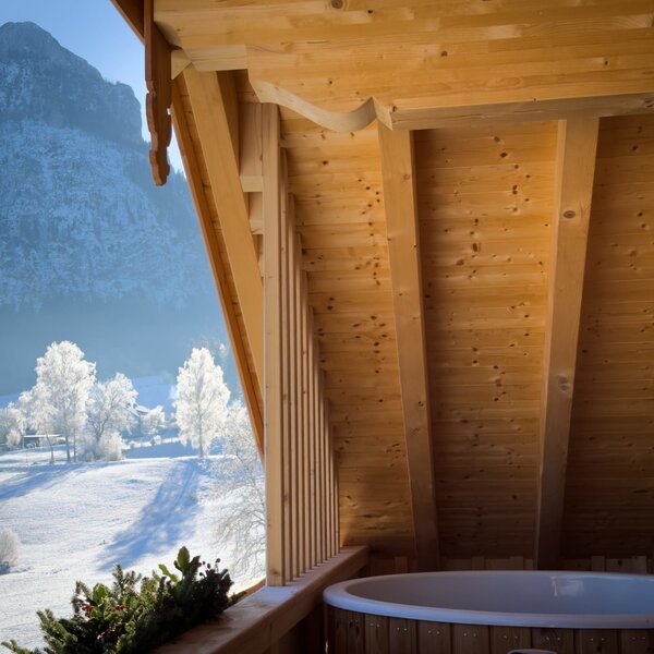 Whirlpool auf dem Holzbalkon des Bauernhofs mit Blick auf die verschneite Berglandschaft.
