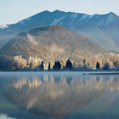 Die Landschaft rund um den Bauernhof mit einem See, raureifbedeckten Bäumen und Bergen.