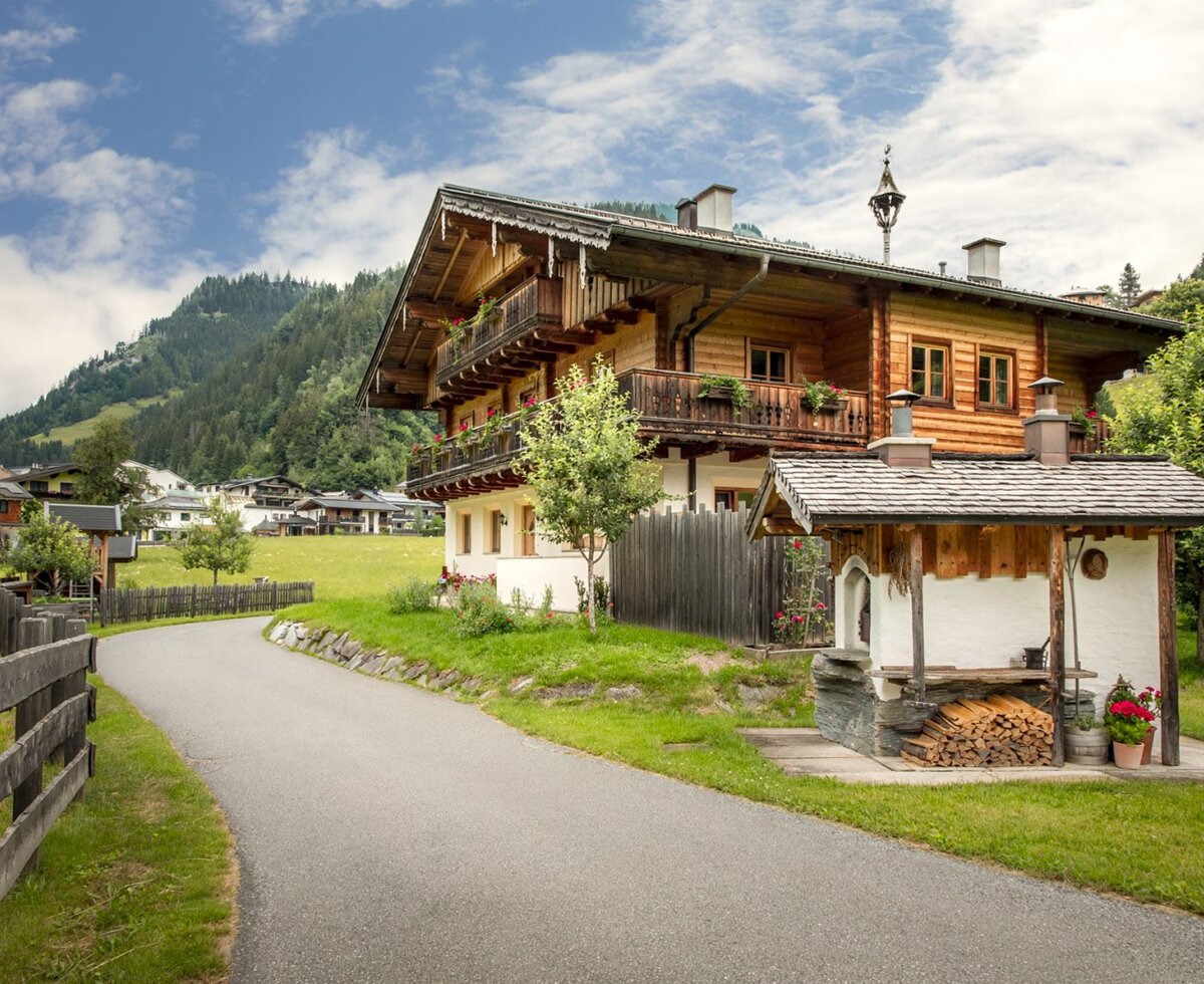 Ein traditioneller Bauernhof aus Holz mit blumengeschmückten Balkonen und einem urigen Ofenhäuschen im gepflegten Garten.