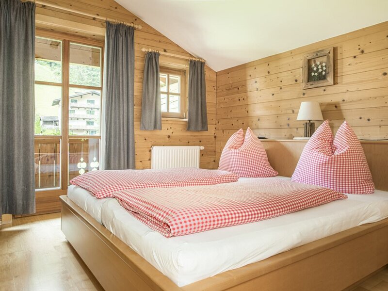 Ein gemütliches Doppelzimmer im Bauernhof mit holzgetäfelten Wänden, rot-weiß karierter Bettwäsche und Balkonzugang.