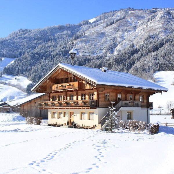 Der Bauernhof mit Holzbalkonen und schneebedecktem Dach, umgeben von winterlichen Bergen.