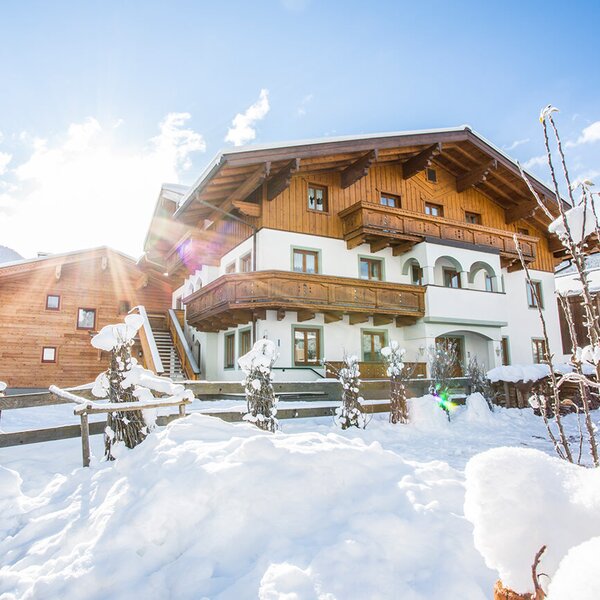 Der Bauernhof mit traditioneller Holzarchitektur und Balkonen, umgeben von Schnee und Bergen im Winter.