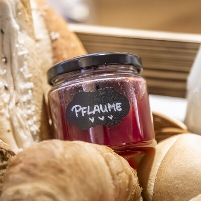 Ein Glas Pflaumenmarmelade, frische Backwaren und Milch als Teil des Frühstücksangebots im Ap­par­te­ments.