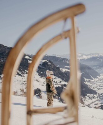 Winterlicher Rodelspaß am Bauernhof mit einer malerischen Aussicht auf die verschneite Berglandschaft.