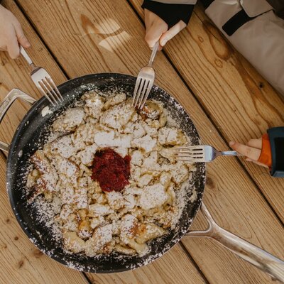 Frischer, mit Puderzucker bestreuter Kaiserschmarrn in einer Pfanne auf dem rustikalen Holztisch des Bauernhofs.