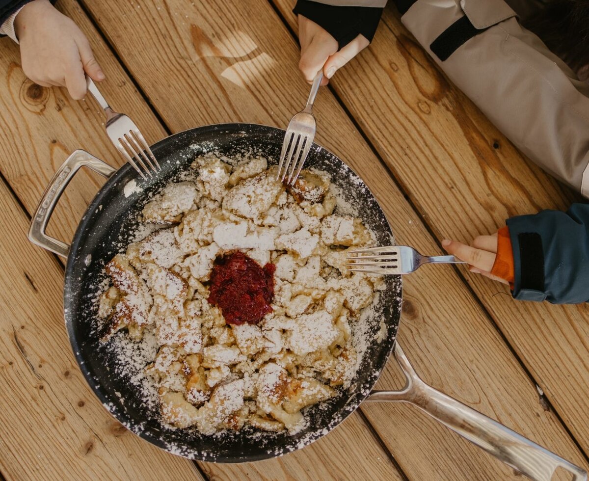 Frischer, mit Puderzucker bestreuter Kaiserschmarrn in einer Pfanne auf dem rustikalen Holztisch des Bauernhofs.