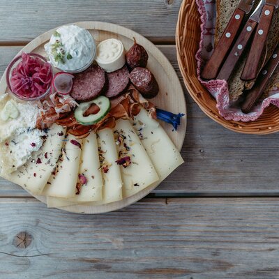 Eine herzhafte Bauernhof-Brotzeit mit einer feinen Auswahl an regionalem Käse, Wurst und frischem Brot auf einem rustikalen Holztisch.