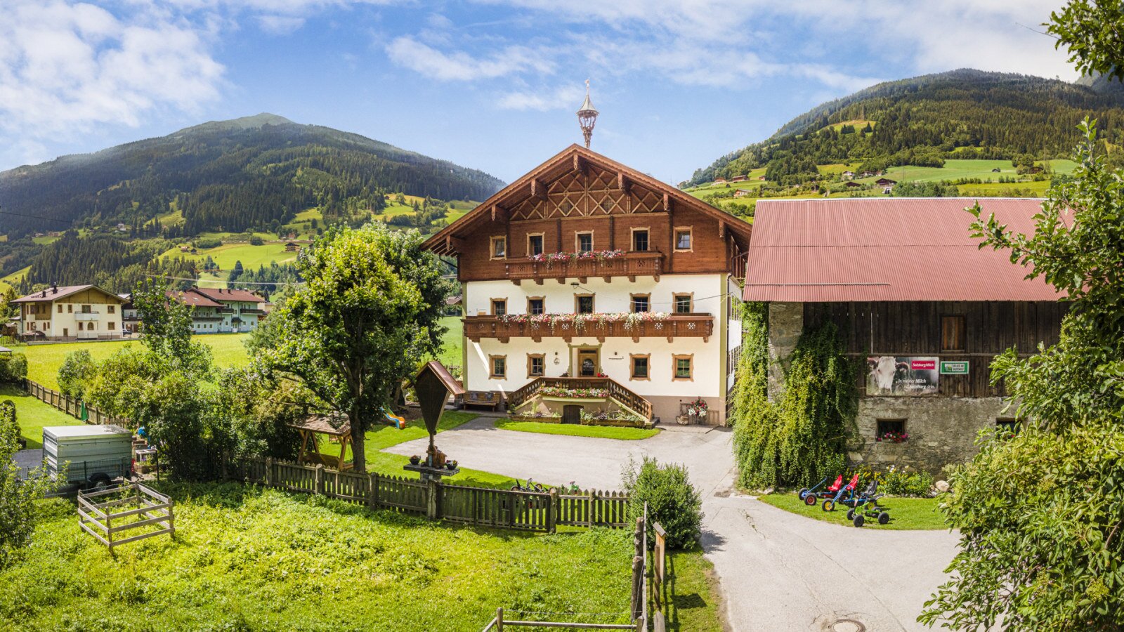 Der einladende Bauernhof im traditionellen Alpendesign, umgeben von einer weitläufigen grünen Wiese und den sanften Berghängen.