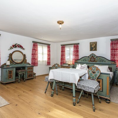 Doppelschlafzimmer im Bauernhof mit Holzboden, Schminktisch, Kleiderschrank und einem kleinen Tisch mit zwei Stühlen.