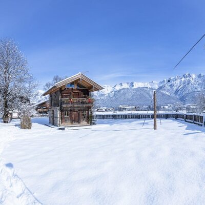 Winterlandschaft des Bauernhofs mit verschneiten Gebäuden und Bergen im Hintergrund.