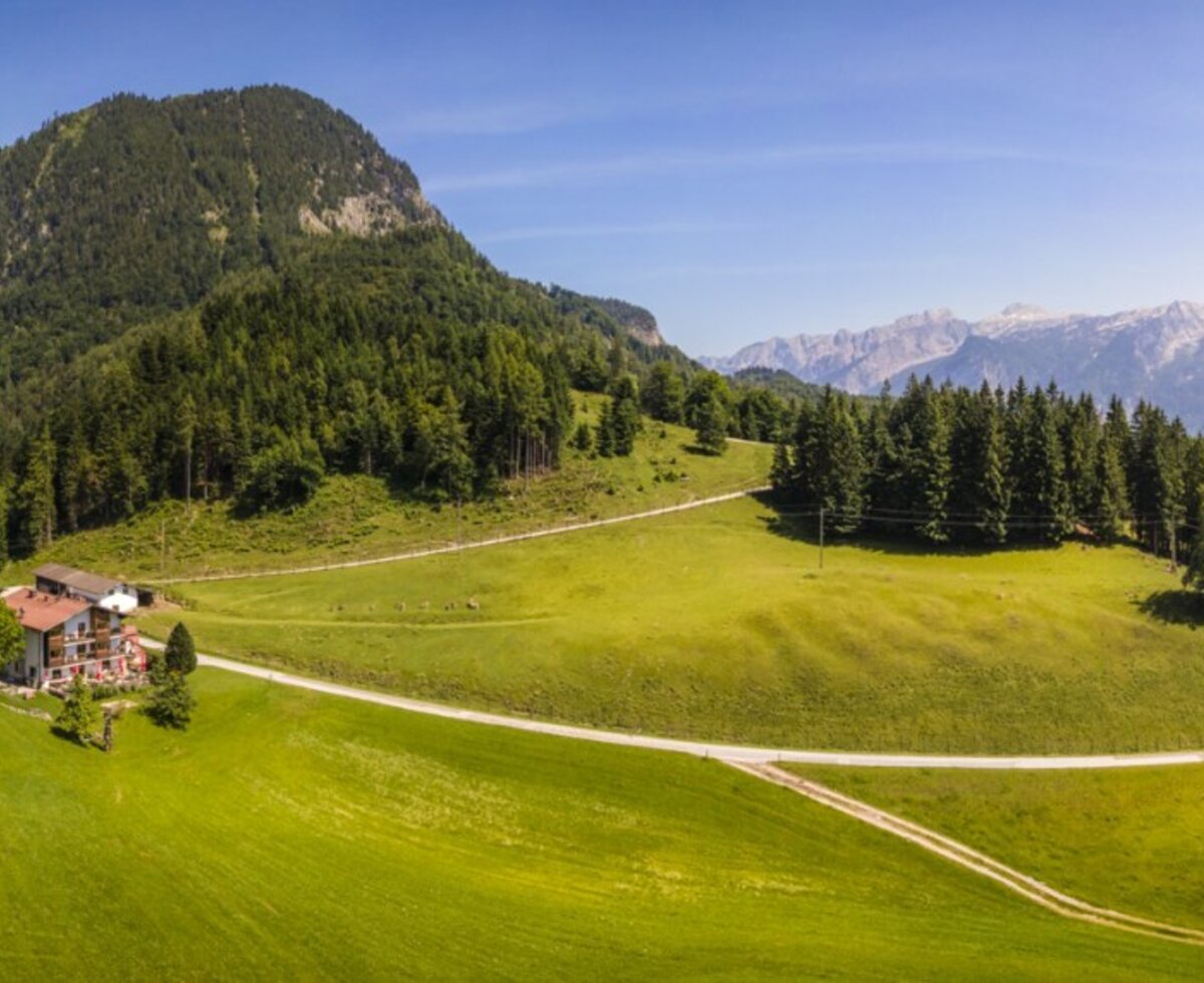 Der Bauernhof ist eingebettet in grüne Wiesen und Wälder mit Panoramablick auf die umliegenden Berge.