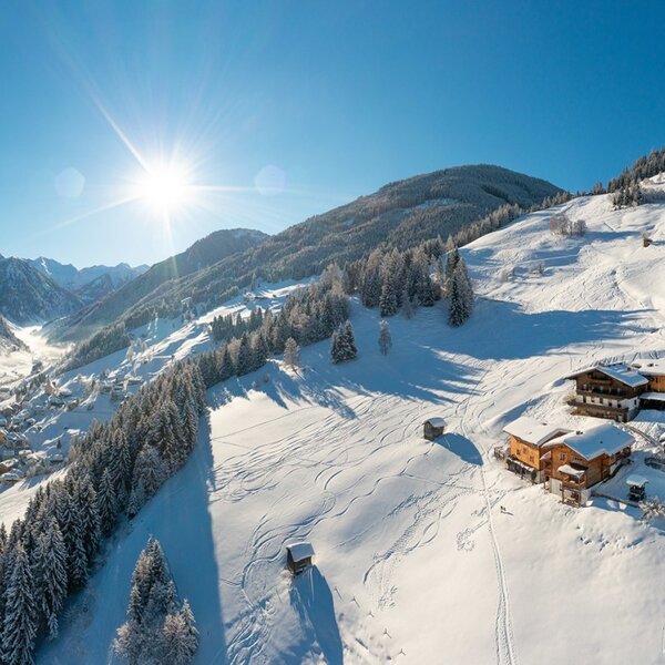 Der Bauernhof in einer verschneiten Winterlandschaft mit Blick auf das Tal und die umliegenden Berge.