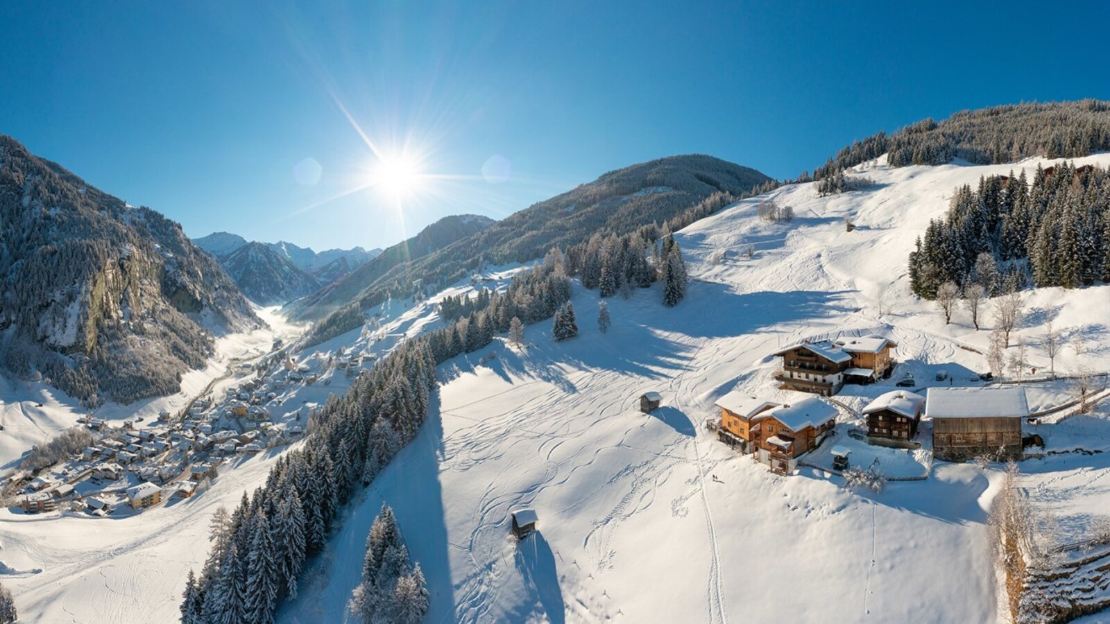 Der Bauernhof in einer verschneiten Winterlandschaft mit Blick auf das Tal und die umliegenden Berge.