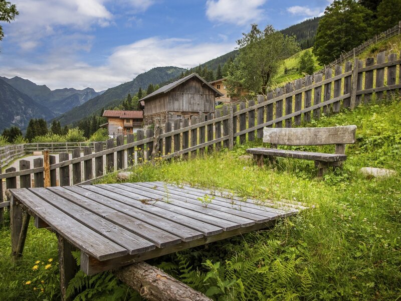 Der einladende Außenbereich des Bauernhofs mit einer rustikalen Holzbank und einem weiten Blick auf die umliegende Berglandschaft.