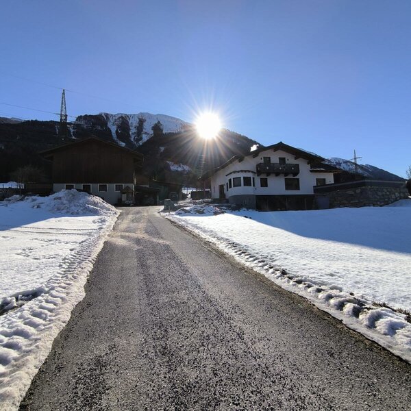 Die Gebäude des Bauernhofs mit einer Zufahrtsstraße, umgeben von Schnee und der winterlichen Berglandschaft.