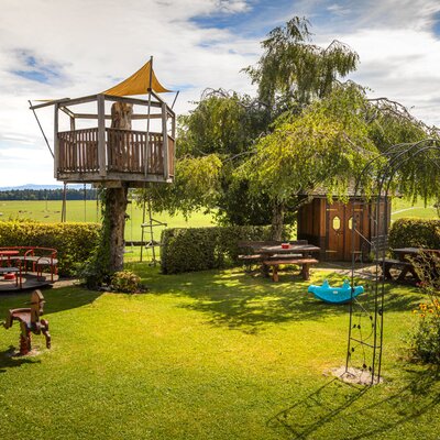 Der einladende Spielplatz des Bauernhofs mit einem hölzernen Baumhaus, verschiedenen Spielgeräten und gemütlichen Sitzbereichen im grünen Garten.