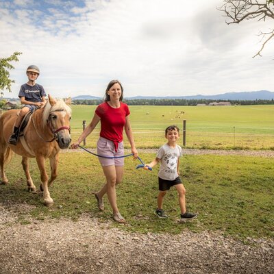Ein aufregendes Ponyreiten für Kinder auf dem einladenden Bauernhof vor einer malerischen Bergkulisse.