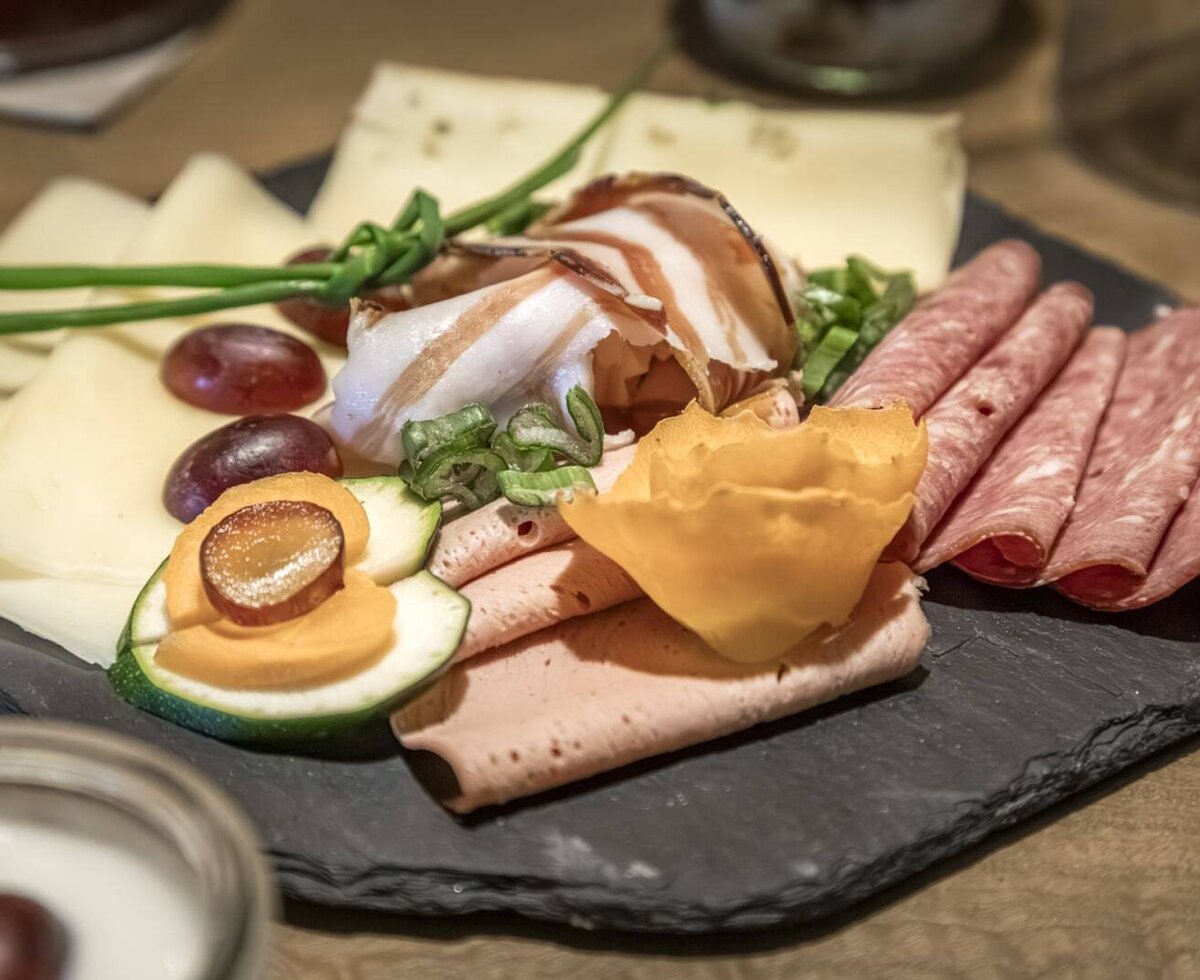 Eine Platte mit Wurst, Käse, Trauben und Gemüse, die zum reichhaltigen Bauernhof-Frühstück im Bauernhof gehört.