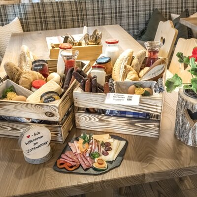 Reichhaltiges Bauernhof-Frühstück mit frischen Backwaren, Aufschnitt, Käse, Marmeladen und Getränken, präsentiert in Holzkörben auf einem Tisch im Bauernhof.