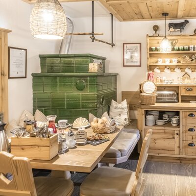Die Bauernstube des Bauernhofs, eingerichtet für das reichhaltige Bauernhof-Frühstück mit einem grünen Kachelofen und Holzmöbeln.